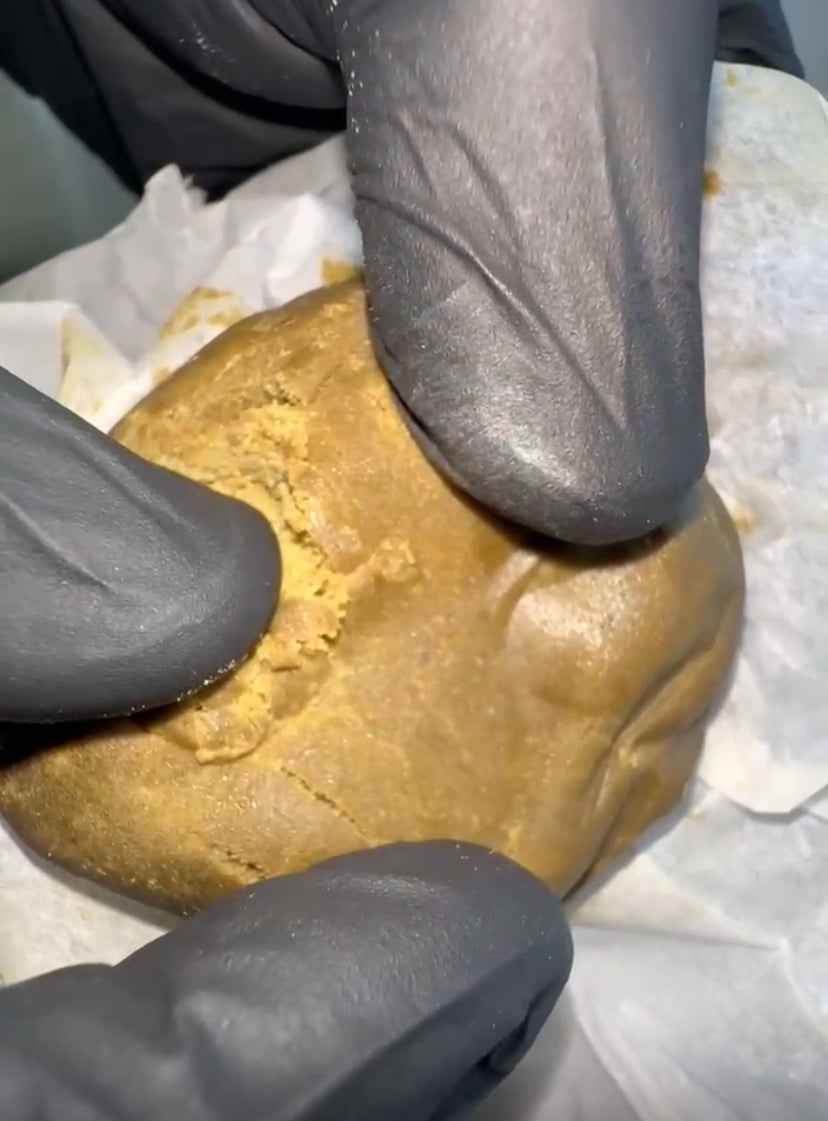 Hash CBD Premium - Hashis Premium di colore dorato consistenza morbida e resinosa, manipolato con guanti neri per garantire qualità e igiene.